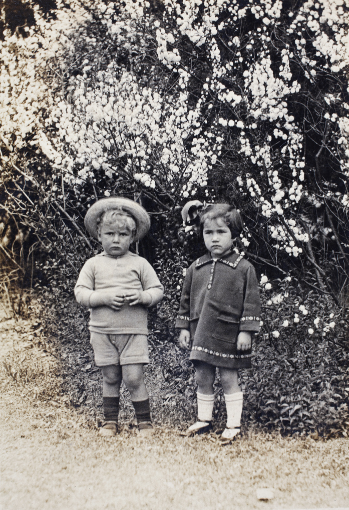 Unidentified boy and girl standing in front of a blooming bush, Shanghai