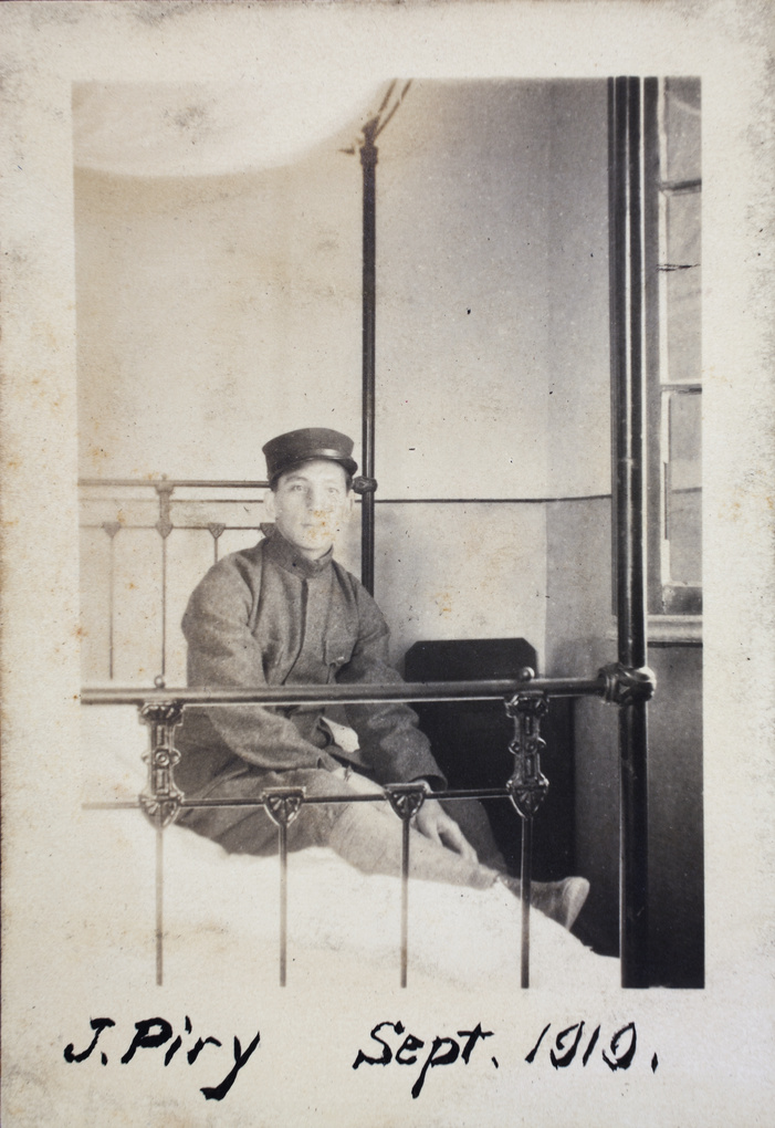 John Piry wearing a military uniform, on an iron-framed bed, 35 Tongshan Road, Hongkou, Shanghai