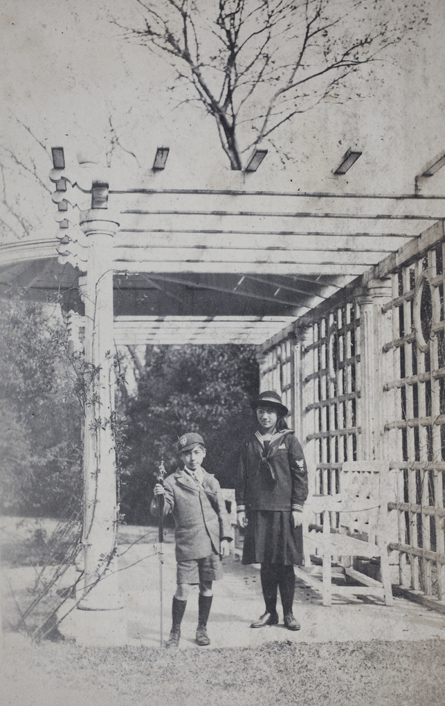 Fred Hutchinson posing with a tripod, standing with Maggie Hutchinson in a park pergola with Doric-style columns, Shanghai