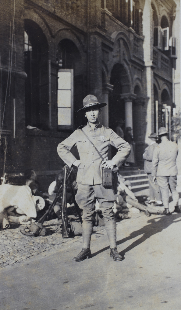 Tom Hutchinson, with his camera case, wearing an American Company uniform in a street with other volunteers, Shanghai