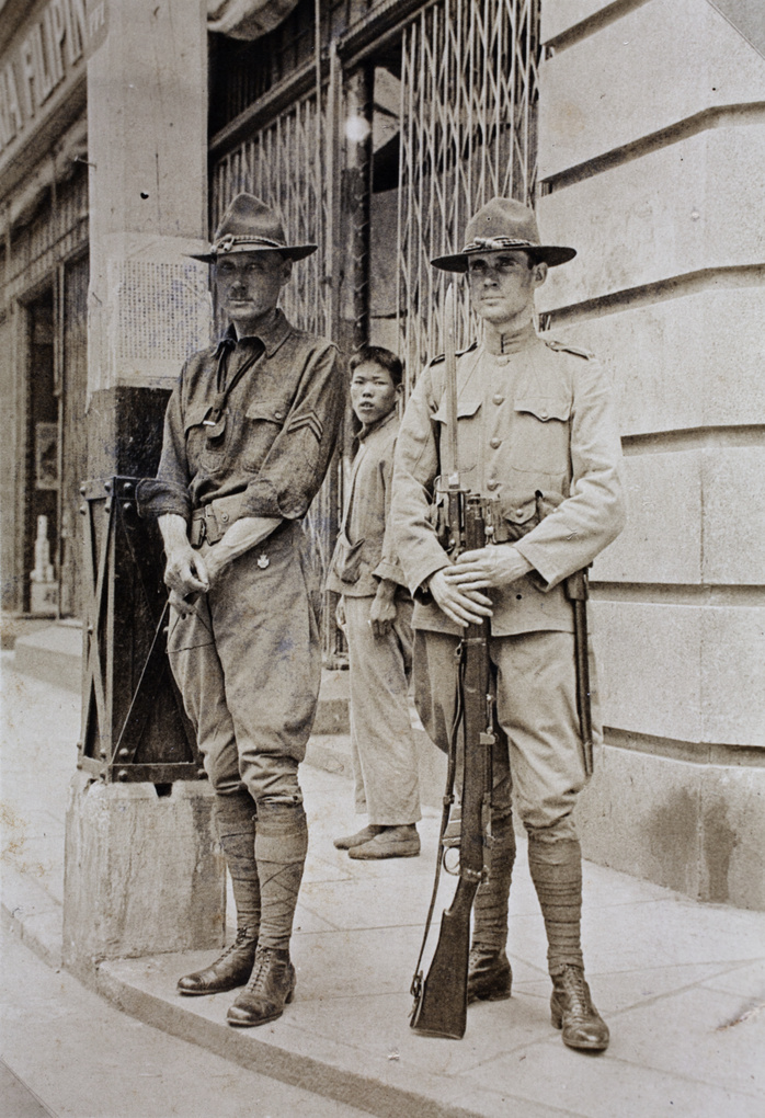 Young man standing behind two American Company Shanghai Volunteer Corps members on a street corner, Shanghai, 1925