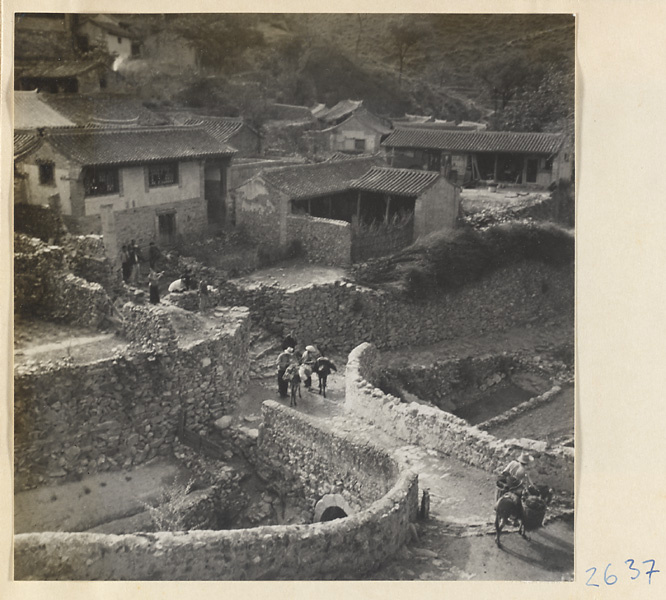 Guides and donkeys crossing a stone bridge in Ta-tsun Village [sic] in the Lost Tribe country