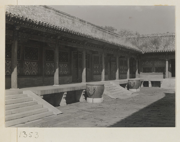 Metal water vats in the courtyard of single-story building with a columnaded porch in the Forbidden City