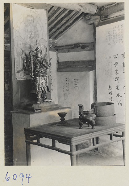 Temple interior showing altar with statue, painting, and hanging scroll at the Xincheng Caves