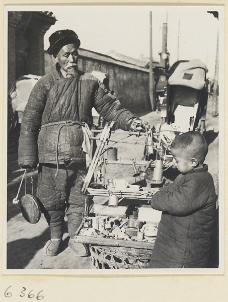 Toy vendor with gong called a tong luo, display stand, and boy holding a toy