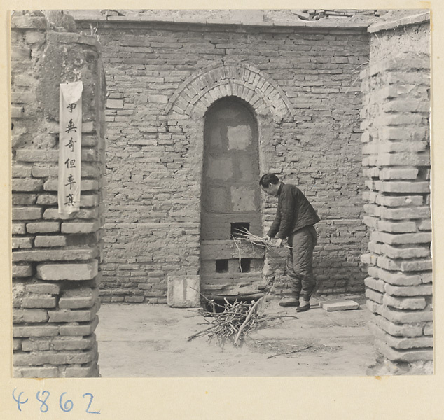 Man adding wood to a kiln next to a wall with an inscription at a tile and brick factory near Mentougou Qu