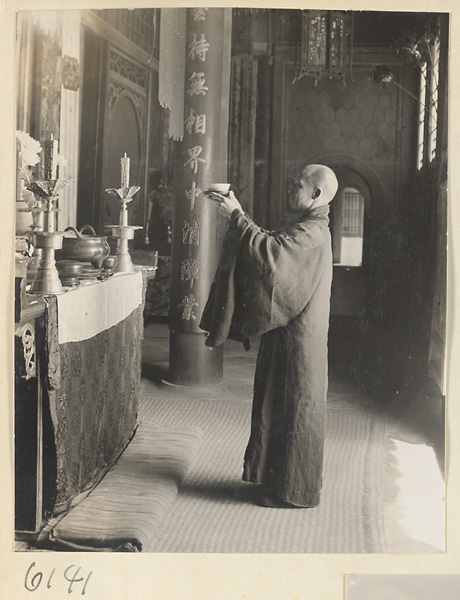 Monk holding up an offering before an altar in a temple