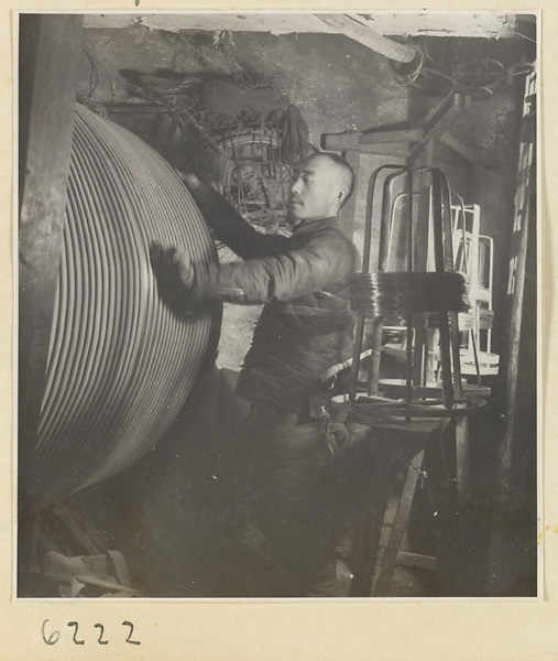 Interior of copper-net factory showing a man working with rolls of copper wire