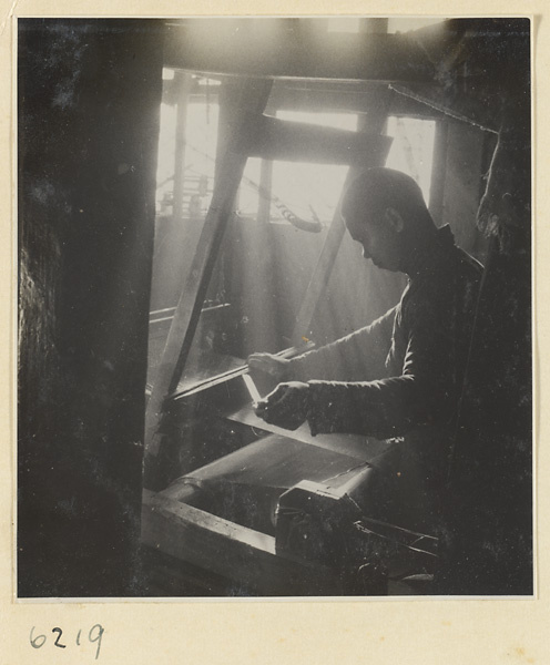 Interior of copper-net factory showing a man working at a loom