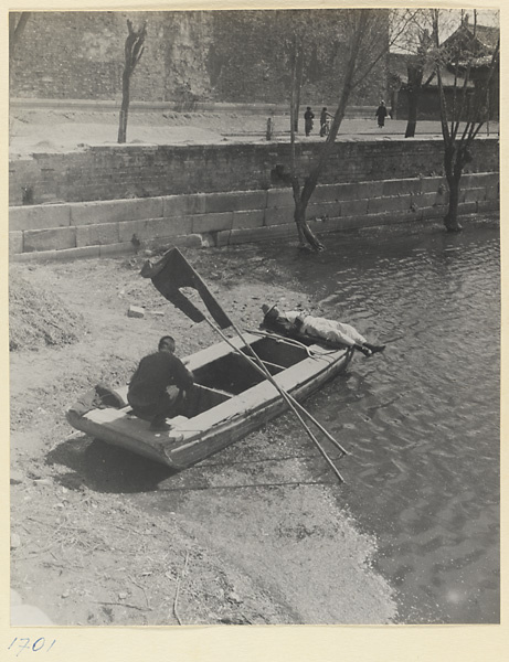 Two men on a boat beached by a city moat