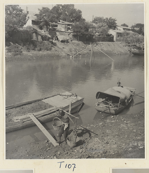 Man carrying baskets onto a boat on the river at Tai'an with frame for a fishing net in background