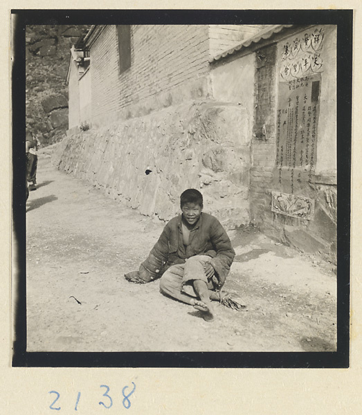 Boy seated below a temple society poster afixed to a building on the pilgrimage trail up Miaofeng Mountain