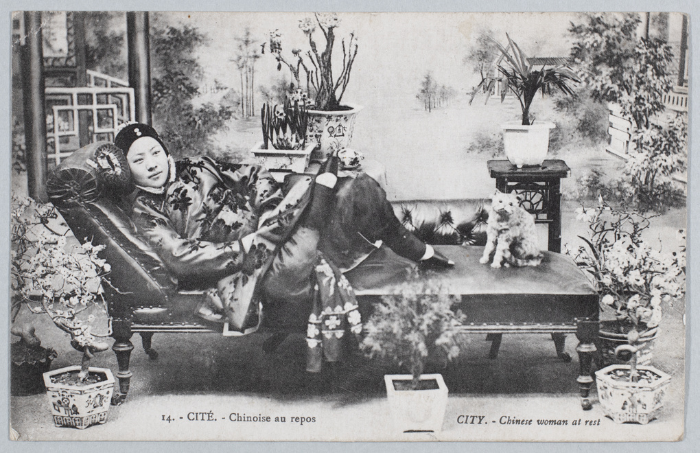 A woman lying on a chaise longue in a photographer's studio, with a stuffed cat