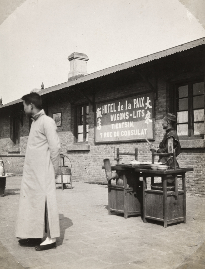 Street food seller on a railway station platform, with sign for the Hotel de la Paix, Tianjin