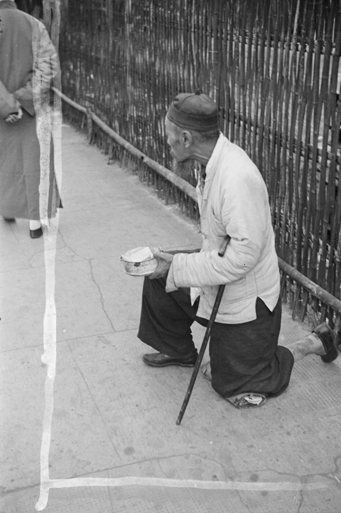 Beggar on bended knee, by bamboo fence, Shanghai