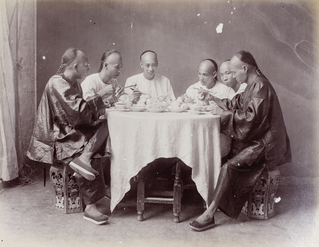A studio tableau of six men having a meal