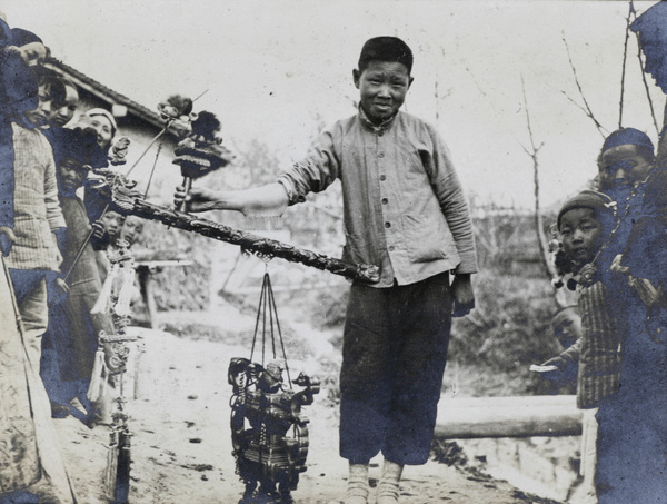 A boy with a weighted pole attached to his forearm by a row of hooks, with onlookers