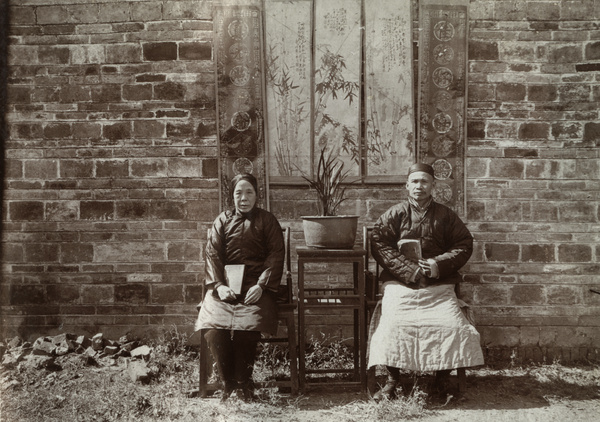 A couple posed with banners, books and a potted plant