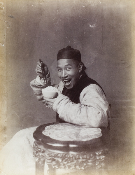 A smiling man posed eating, in a photographer's studio