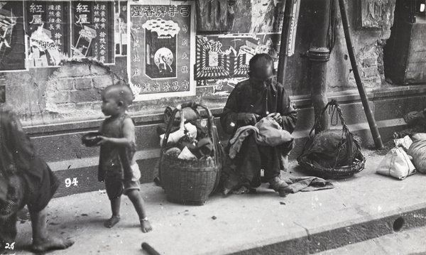Pavement scene: a seamstress sewing and a toddler begging, Hong Kong