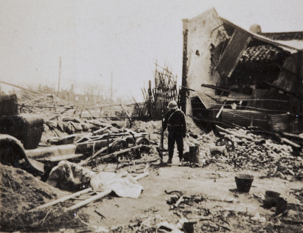Japanese soldier standing by the wreckage of a bus, Shanghai, 1932