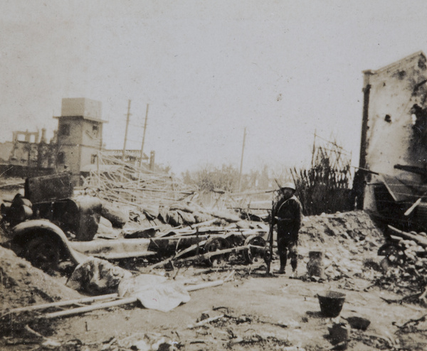 Japanese soldier standing beside a wrecked bomb bus, Shanghai, 1932