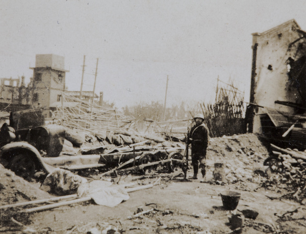 Japanese soldier standing beside a wrecked bomb bus, Shanghai, 1932