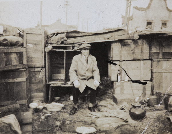 A man beside a shelter made from packing crates, Zhabei, Shanghai, 1932