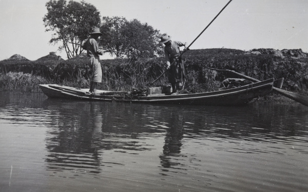 Two men working in a boat near grave mounds