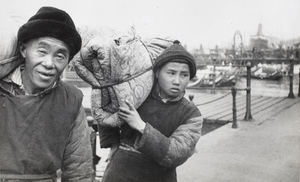 Two men with bundles near a pier