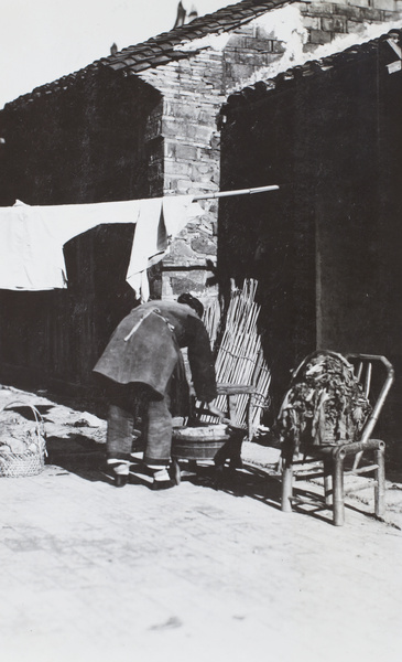 Woman with bound feet washing clothing in a laundry tub