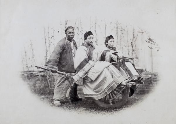Wheelbarrow man with two women wearing fine clothing