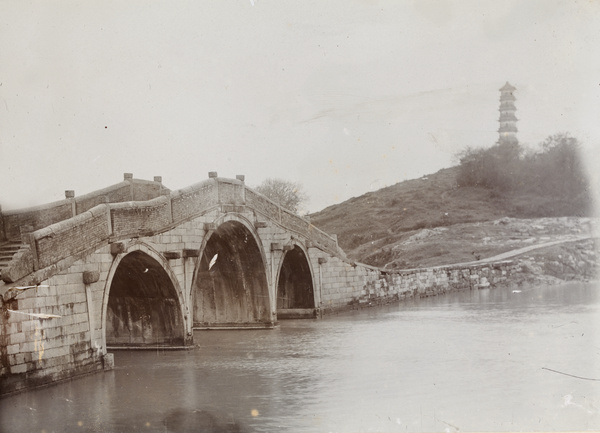 A three-arch stone bridge near a pagoda