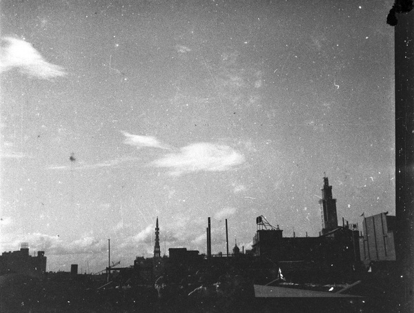 Soldiers watching a military aeroplane in the sky above department store towers, Shanghai, August 1937