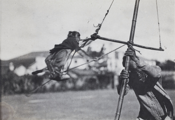 Travelling street entertainer spinning a performing monkey tethered to a pole