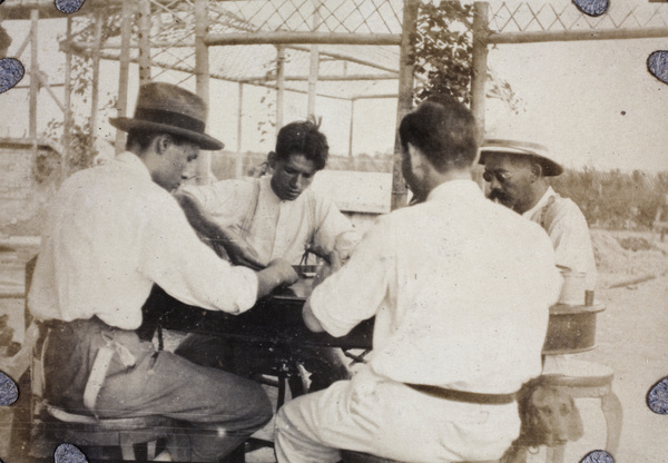 Four men playing mahjong under a pergola in the garden of T. J. Roche, Shanghai