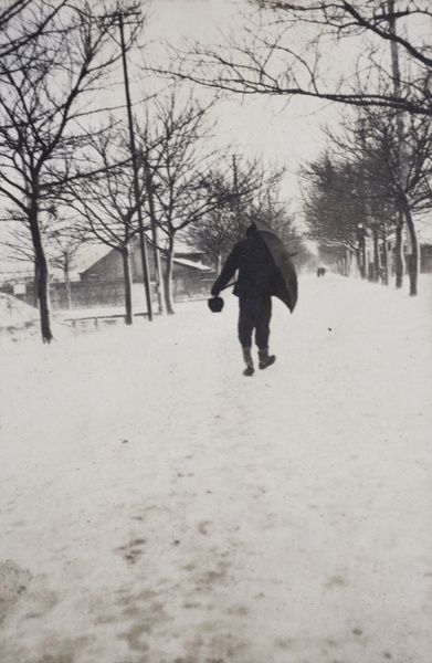 Man walking along snow covered Tongshan Road, sheltering behind an umbrella from winter weather, Hongkou, Shanghai, February 1919