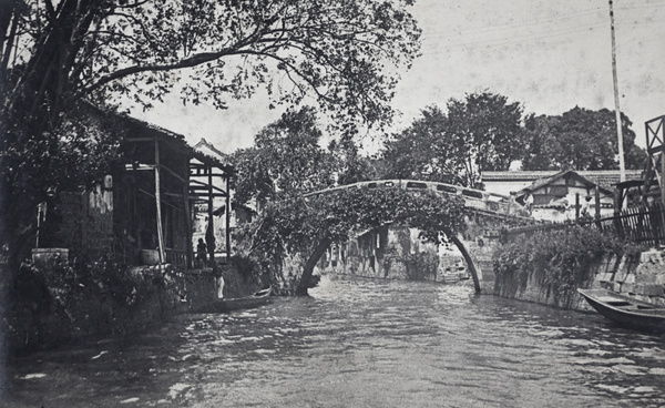 Waterside dwellings and a bridge photographed from a boat travelling along a waterway, near Hangzhou