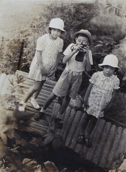 Jim Hutchinson holding a camera to his eye, with two unidentified girls