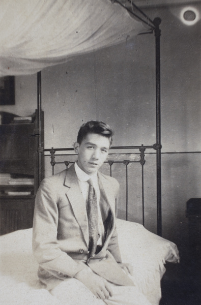 Bill Hutchinson sitting on an iron-frame bed, 35 Tongshan Road, Hongkou, Shanghai 