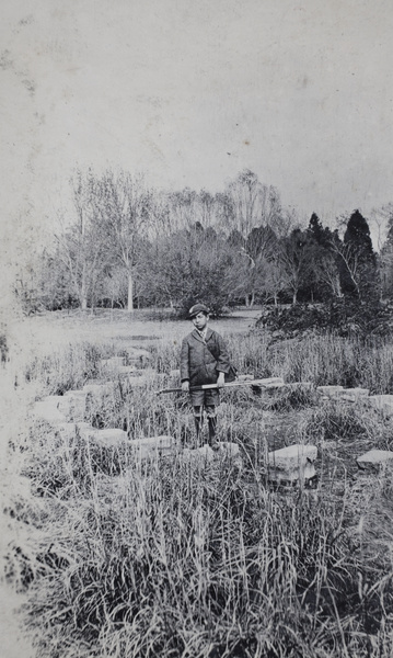 Fred Hutchinson, with a camera box and tripod, standing on stepping stones in a park, Shanghai