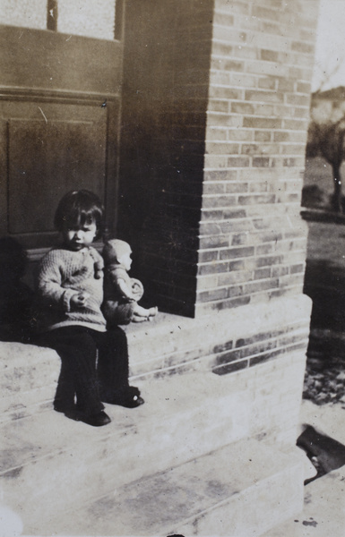 Bea Hutchinson holding a doll and sitting on the verandah steps, 35 Tongshan Road, Hongkou, Shanghai