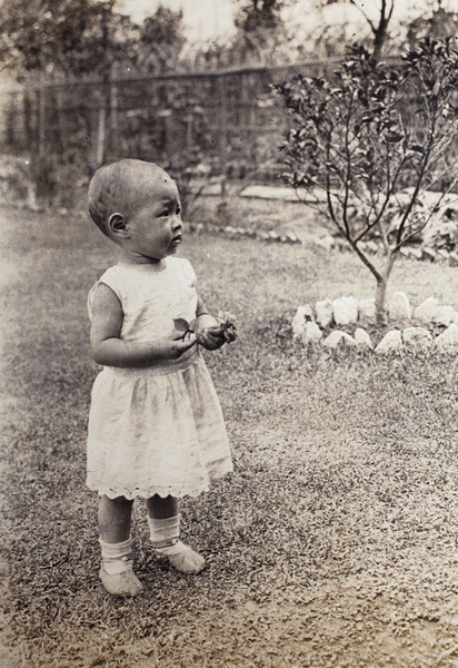Gladys Hutchinson holding a rose blossom and standing in the garden, 35 Tongshan Road, Hongkou, Shanghai