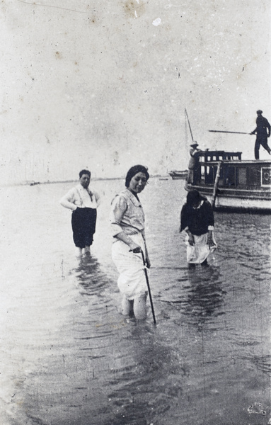 Unidentified women and a man wading in the water near a houseboat