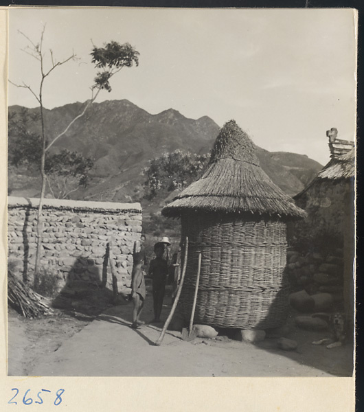 Courtyard with children, stone wall, and round structure made of plant fiber in the Lost Tribe country