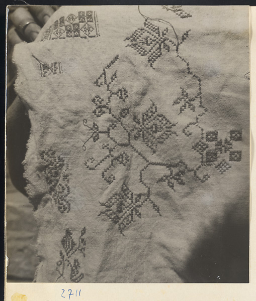 Woman holding up a piece of cross-stitch embroidery in Lo-pu-ch'iao Village [sic] in the Jumahe Valley