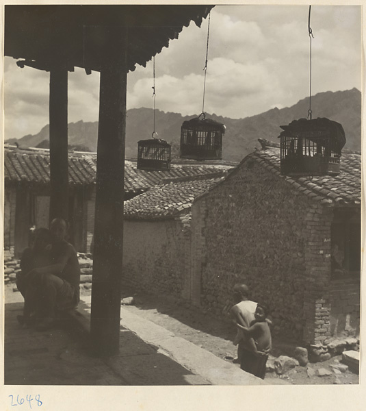 View of houses, villagers, and birdcages hanging from the roof of a community building with a threshing floor in Sang-yuan Village [sic] in the Lost Tribe country