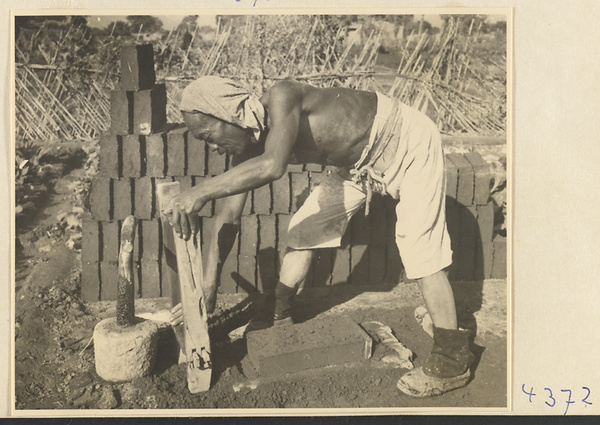 Man removing the mold from a newly-formed brick at a brick factory near Baoding