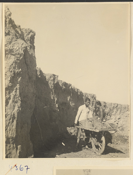 Man pushing a wheelbarrow filled with clay at a brick factory near Baoding