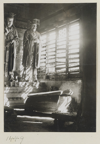 Coffin in front of two shrine figures, one holding a stalk of grain, one wearing a mian liu hat, at Da Fo si